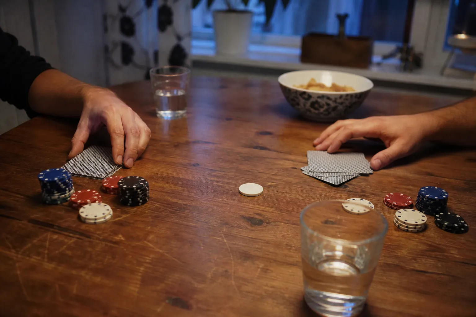 Hemmapoker vid ett träbord med spelmarker, vattenglas och en skål snacks